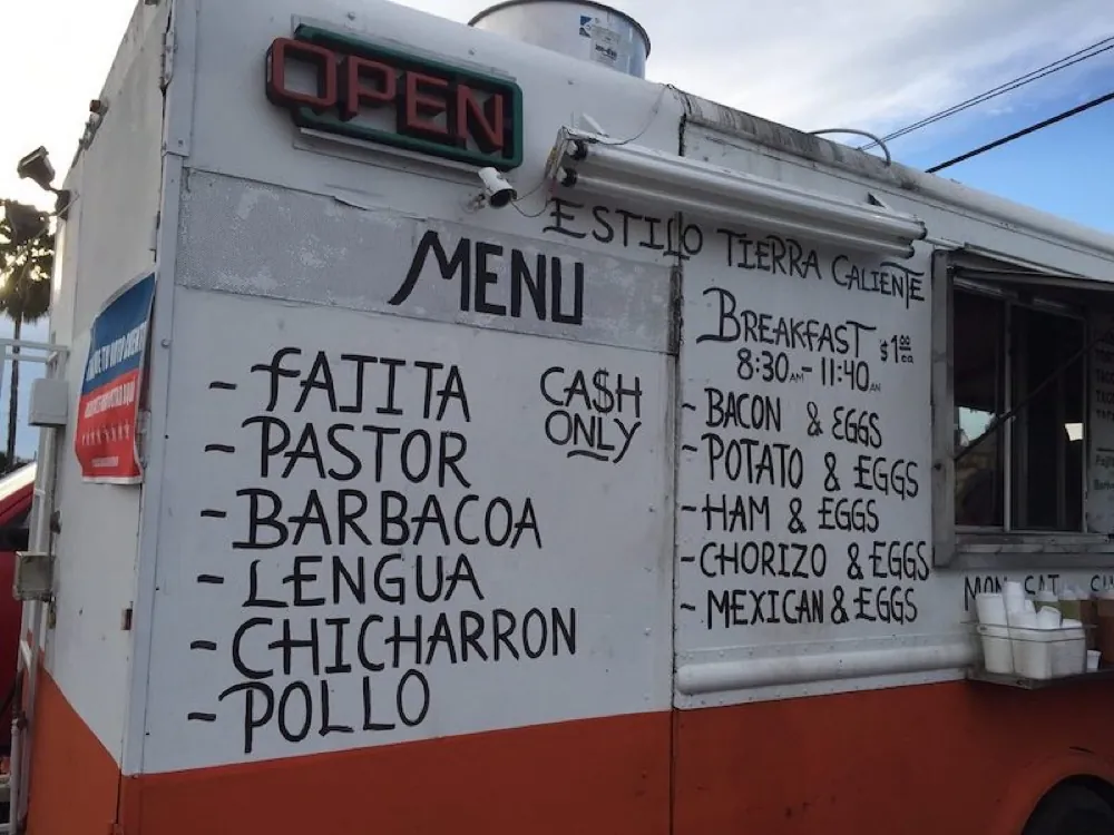 The hand-painted menu board on the Tacos Tierra Caliente truck listing fajita, pastor, barbacoa, lengua, chicharrón, pollo and breakfast tacos — cash only